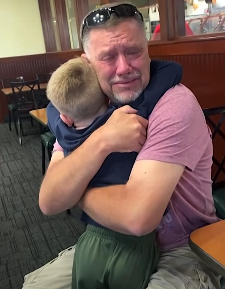 A deeply emotional grandfather hugs his young grandson tightly at a restaurant. Tears stream down his face as he holds the child close, overwhelmed with love.