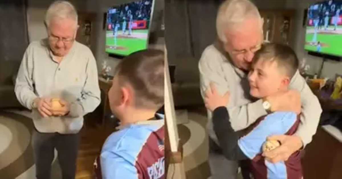 An elderly man looks emotionally touched as he receives a special baseball from a young boy in a sports jersey, followed by a heartfelt hug between the two.