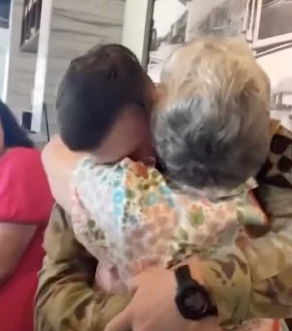 A heartwarming moment as a grandmother tightly embraces her grandson in uniform after being surprised. Both appear emotional, highlighting their deep bond and the joy of reunion.