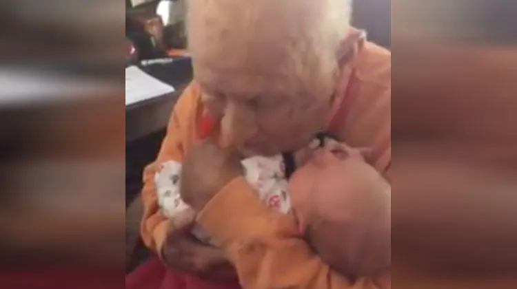 Old man tenderly holds a newborn baby against his chest, eyes closed in a peaceful, emotional moment.