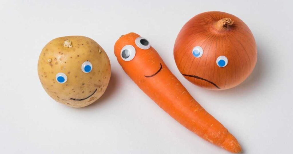 A potato, a carrot, and an onion are arranged with googly eyes and drawn-on faces; the potato and carrot are smiling, while the onion has a sad expression—representing a humorous setup for fun and harmless pranks involving vegetables.