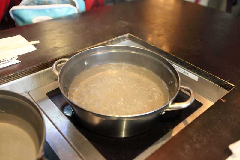 A metal pot of water boiling on a stovetop with steam rising from the surface.
