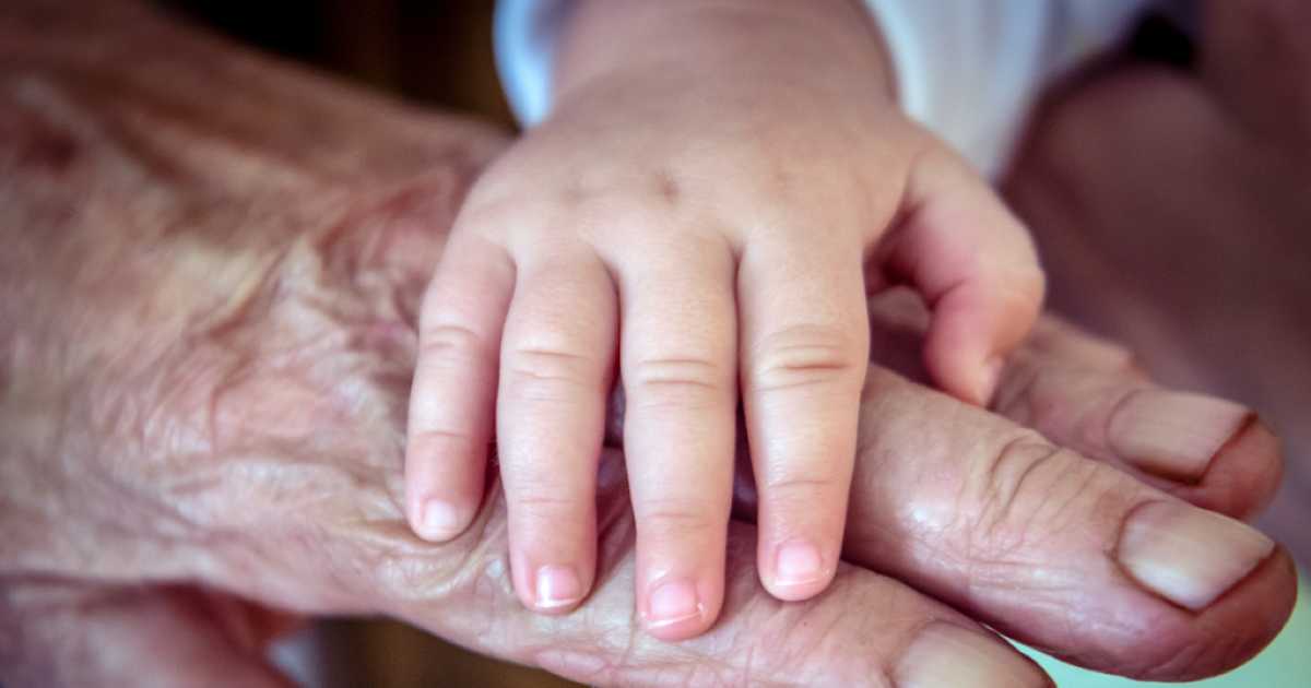 A close-up of a young child’s hand gently resting on top of an elderly person’s wrinkled hand, symbolizing love, connection, and generations coming together.