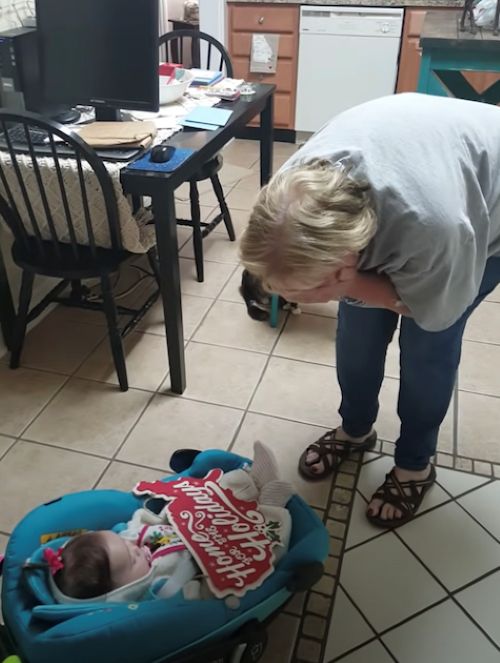 Woman bends over joyfully to greet baby in a carrier, still holding the “Home for the Holidays” sign.