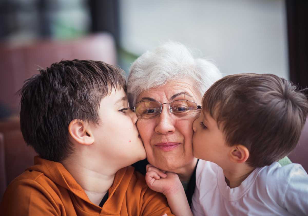 Elderly woman with glasses gets kissed on both cheeks by two young boys.