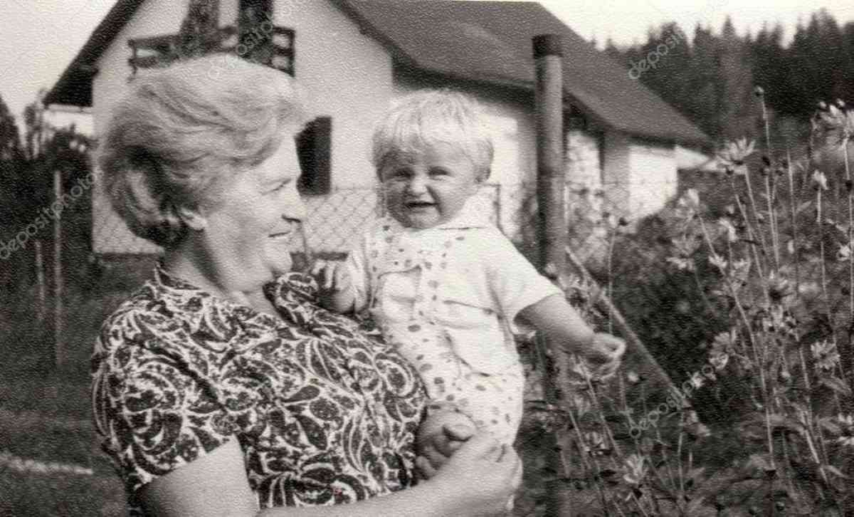 Vintage black and white photo of a smiling grandmother holding a toddler in a garden.