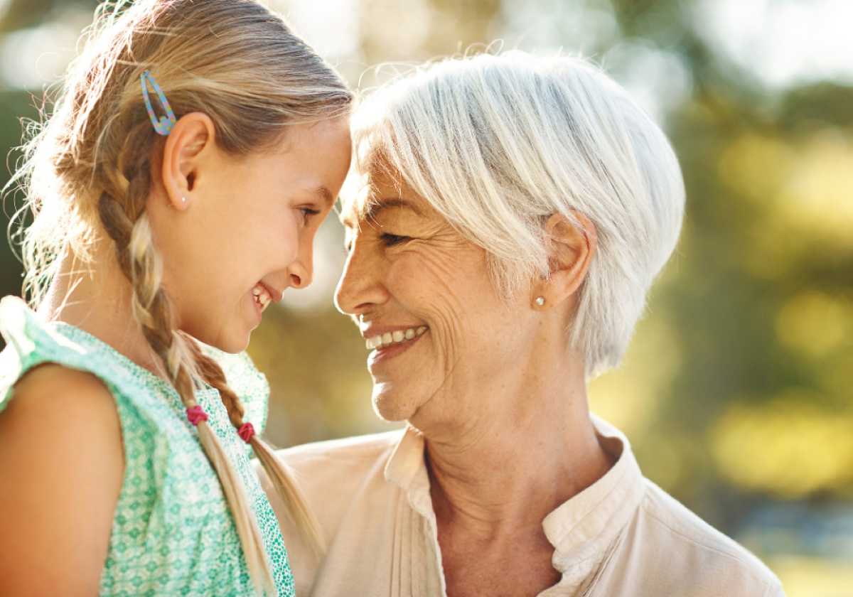 Smiling grandmother and granddaughter touch foreheads lovingly while sharing a joyful moment outdoors.
