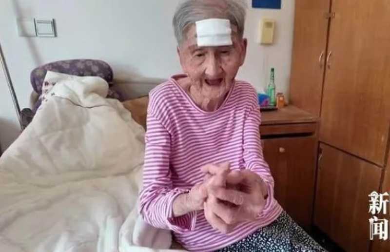 Elderly woman with a bandage on her forehead, sitting up in bed and wearing a striped pink shirt.