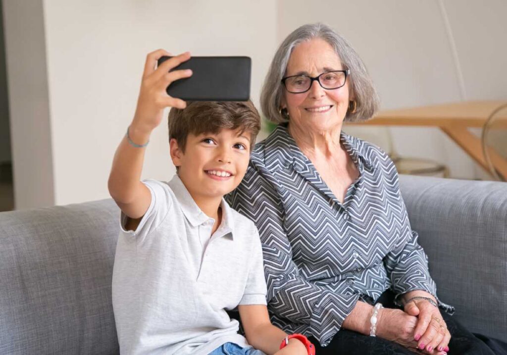 Smiling boy takes a selfie with his grandmother while sitting together on a couch.