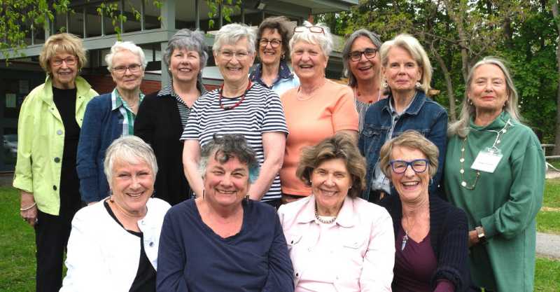 Group of cheerful older women pose together outdoors, smiling and enjoying a friendly gathering.