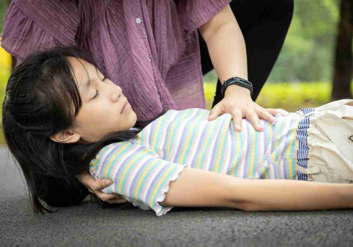 Person checks on an unconscious girl lying on the ground, possibly providing first aid.