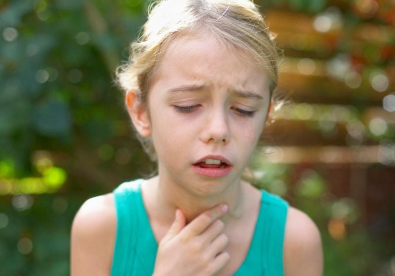 Young girl holding her throat in discomfort, possibly experiencing throat pain or difficulty breathing.