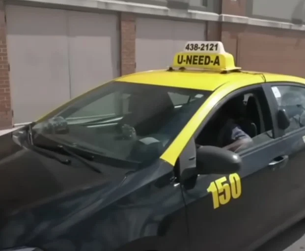 Black and yellow taxi with the sign "U-NEED-A" parked on a city street, marked with the number 150.