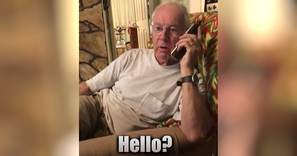 Older man in glasses sitting on a couch, holding a cordless phone to his ear with a surprised expression and the word “Hello?” on the screen.
