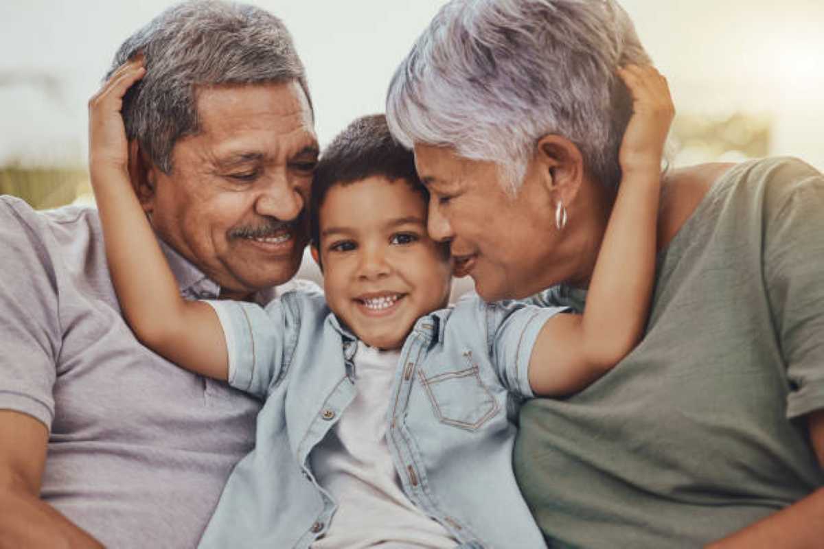A joyful child sits between two adults, all showing affection as they share a warm, loving moment together outdoors.