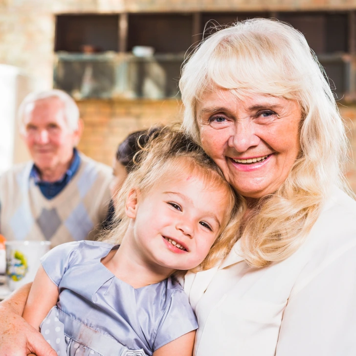 Happy grandmother hugs her smiling granddaughter while sitting together at a family gathering.