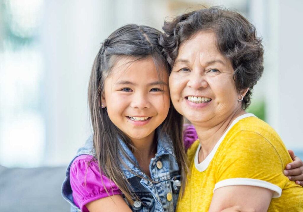 Smiling grandmother and granddaughter pose closely together, both looking at the camera.