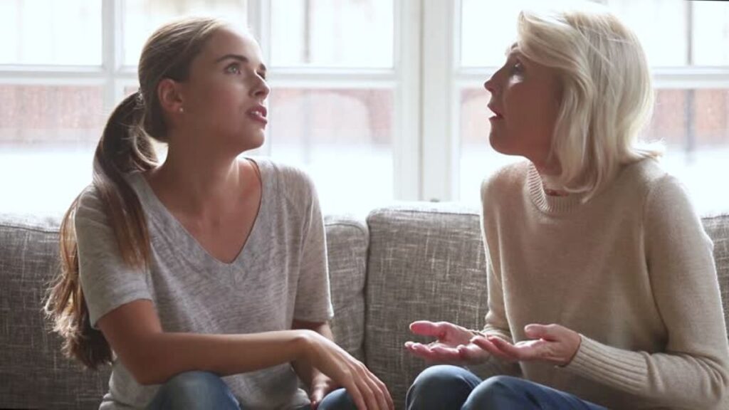 9 Emotional Wounds Adult Children Simply Don’t Realize They’re Inflicting on Their Parents 2 Two women sitting on a couch having a serious conversation near a bright window.