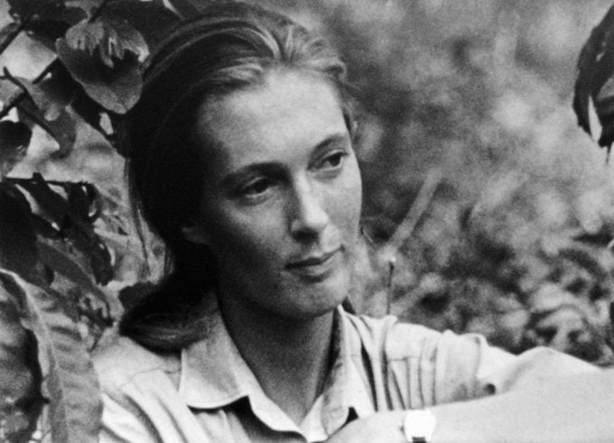 Black-and-white photo of a woman sitting in nature, gazing thoughtfully, surrounded by plants.