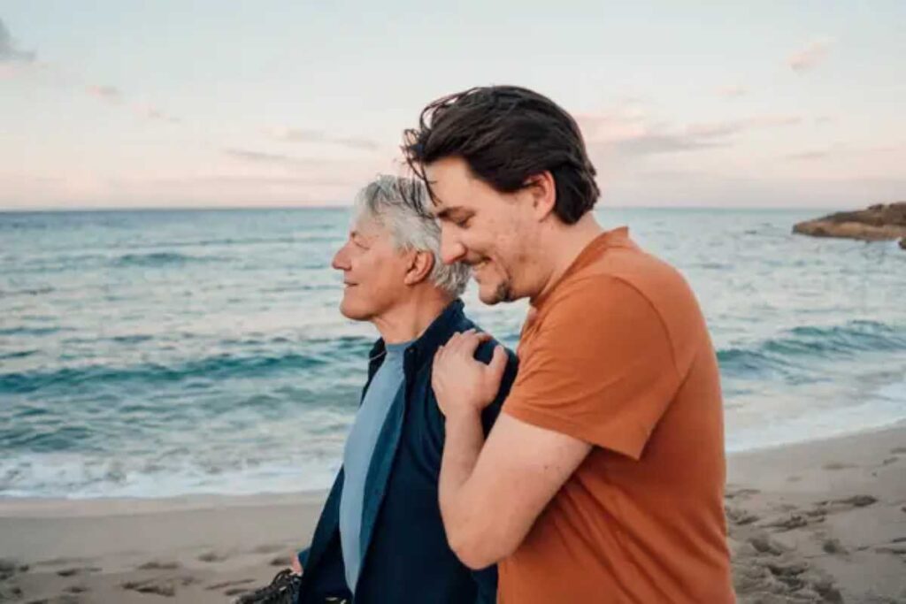 These are the 6 phrases adult children still want to hear from their parents, experts agree 2 Older man and younger man walk side by side on the beach, smiling and enjoying a peaceful moment by the ocean.