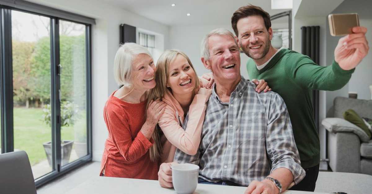 A smiling family gathers around a table, with a cozy living space and large windows overlooking a lush garden.