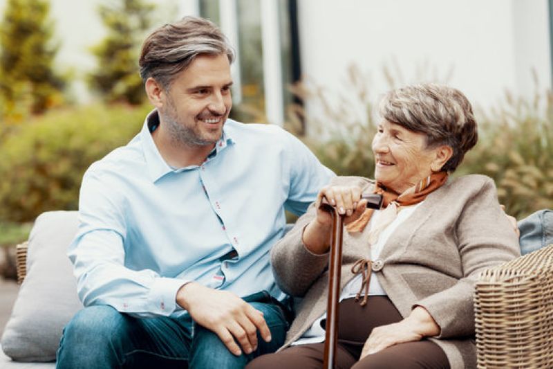 Middle-aged man smiling while chatting with an elderly woman holding a cane on a patio.