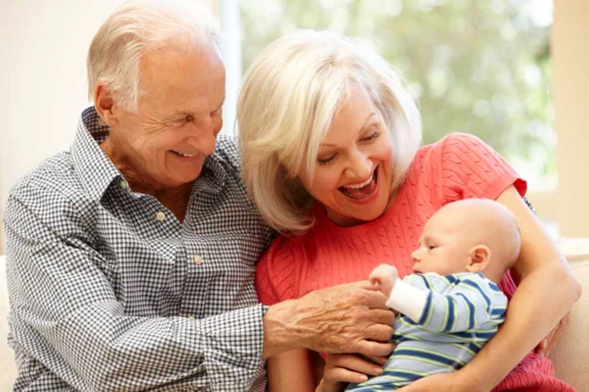 Happy grandparents smiling and playing with a baby in a bright, cozy room.