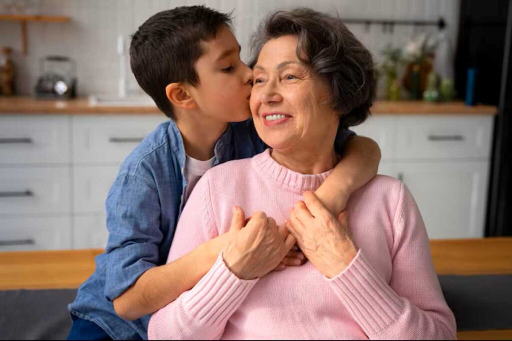 Every Grandma Should Say This One Thing to Their Grandchildren Before the New Year Begins 2 A child embraces an elderly woman in a cozy kitchen setting, sharing a warm moment together.