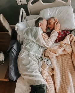 Granddaughter captures the powerful last moments of grandparents’ 60-year love story 2 Wide view of an elderly couple resting together in a hospital bed, wrapped in blankets and holding each other, symbolizing enduring love at the end of life.