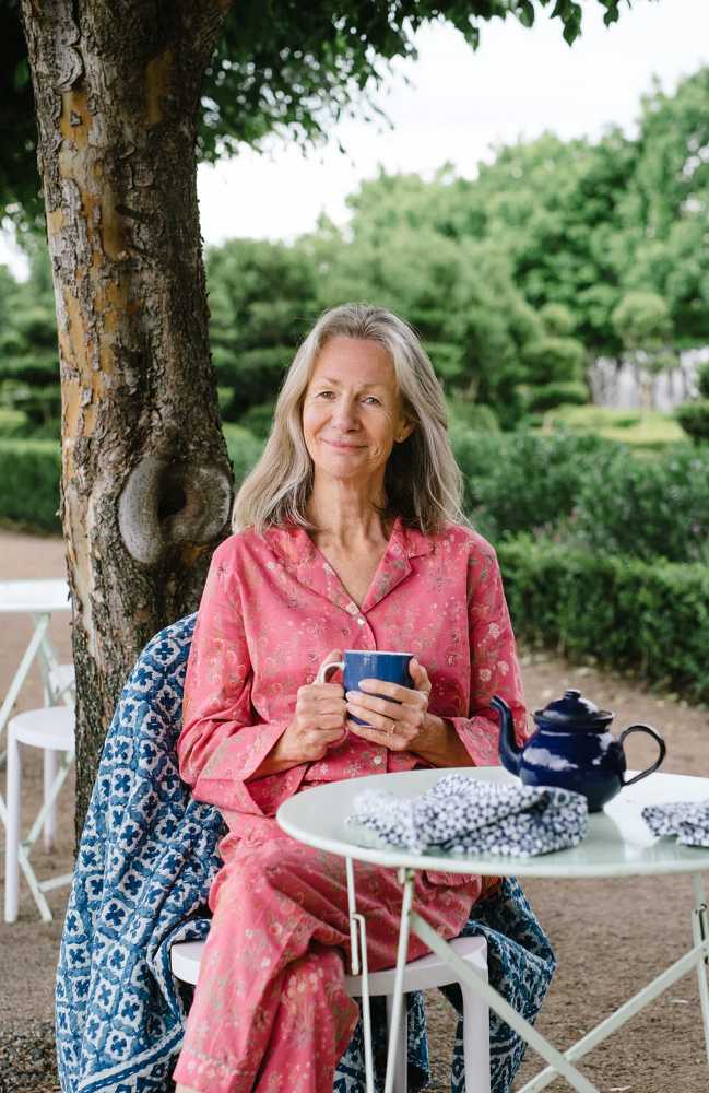 If you want to be happier after 60, eliminate these 5 harmful things from your life 2 Older woman sitting at a small outdoor table holding a cup of tea, surrounded by greenery, enjoying a quiet, relaxed moment of reflection and simple happiness.