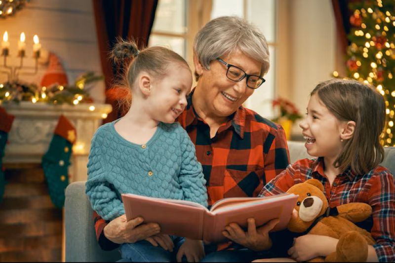 25 Simple Christmas Traditions You Can Start This Year That Grandkids Never Forget 2 A person reads to two children on a cozy couch, surrounded by festive decorations, a Christmas tree, and holiday lights.