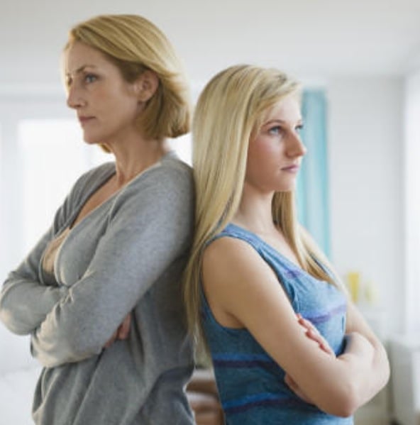 Adult daughter and older mother standing back to back with arms crossed, both looking away, showing emotional distance and unresolved tension between them.