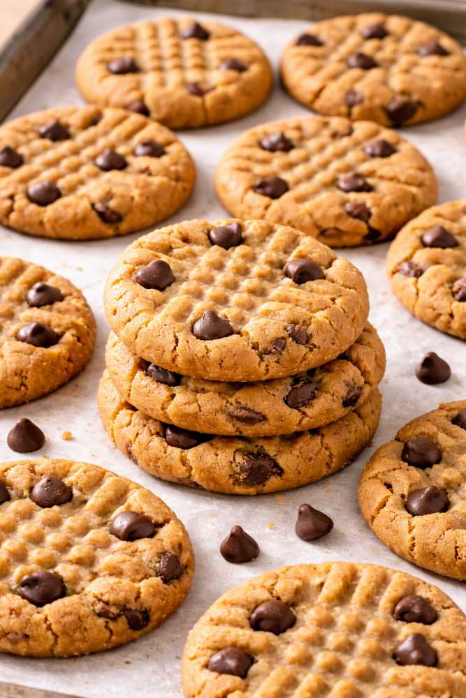 The Best 3-Ingredient Peanut Butter Cookies Recipe You’ll Ever Make 5 Peanut butter cookies baked with chocolate chips, stacked and surrounded by more cookies on a parchment-lined baking sheet.