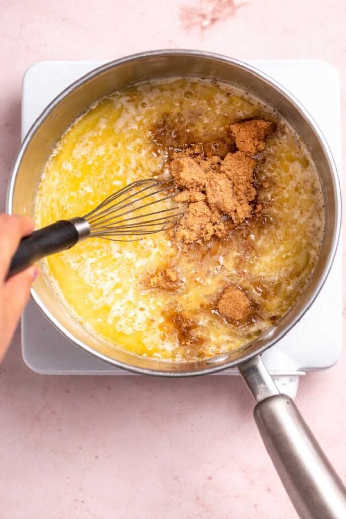 Super Velvety 3-Ingredient Peanut Butter Fudge Recipe You’ll Crave Again and Again 3 Melted butter and brown sugar being whisked together in a saucepan on a stovetop during fudge preparation.