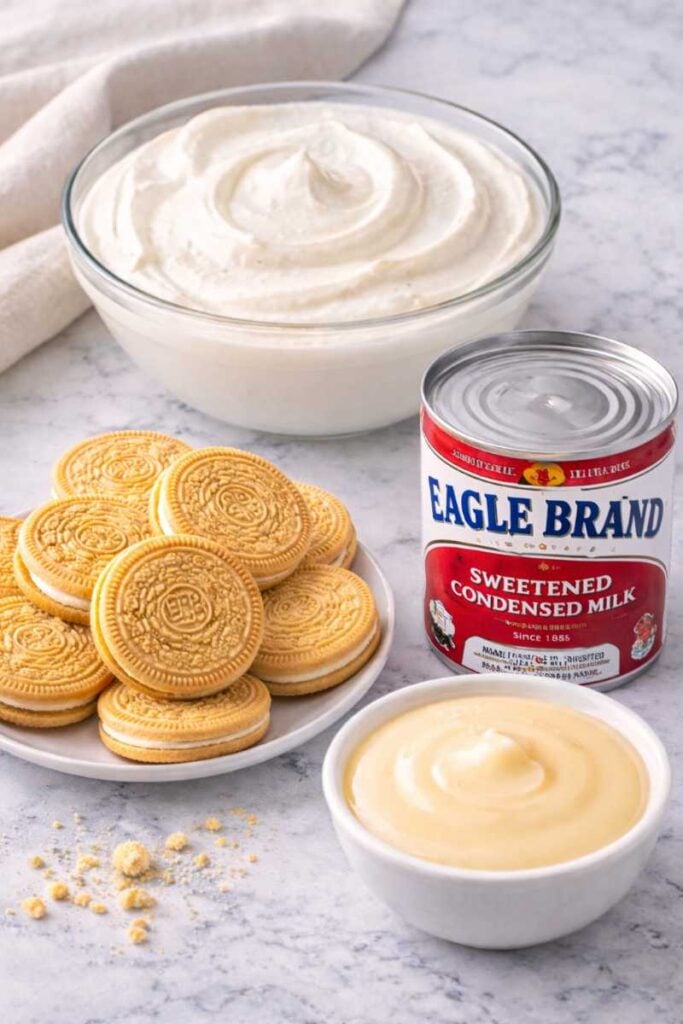 The Best 3-Ingredient Greek Yogurt Cheesecake Recipe Ever (No Bake With Condensed Milk) 2 Ingredients for no-bake Greek yogurt cheesecake including vanilla sandwich cookies, sweetened condensed milk, and whipped Greek yogurt in a glass bowl.