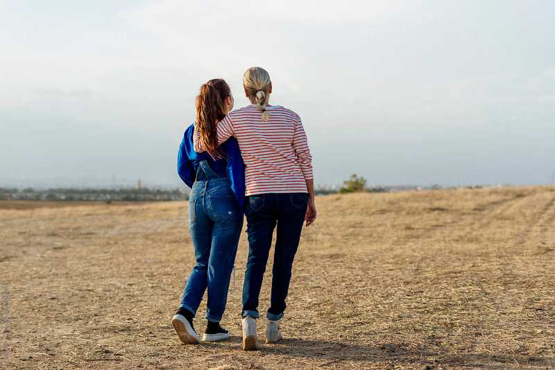 6 Nice Things to Say to Your Teen Granddaughter (That She’ll Never Forget) 3 Teen girl and older woman walking arm in arm across an open field, seen from behind.