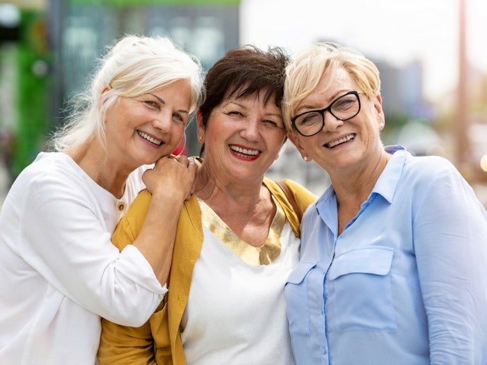Psychology says people raised in the 1960s and 70s developed these 7 mental strengths that are rare today 3 Three older women standing close together and smiling warmly while enjoying time outside.
