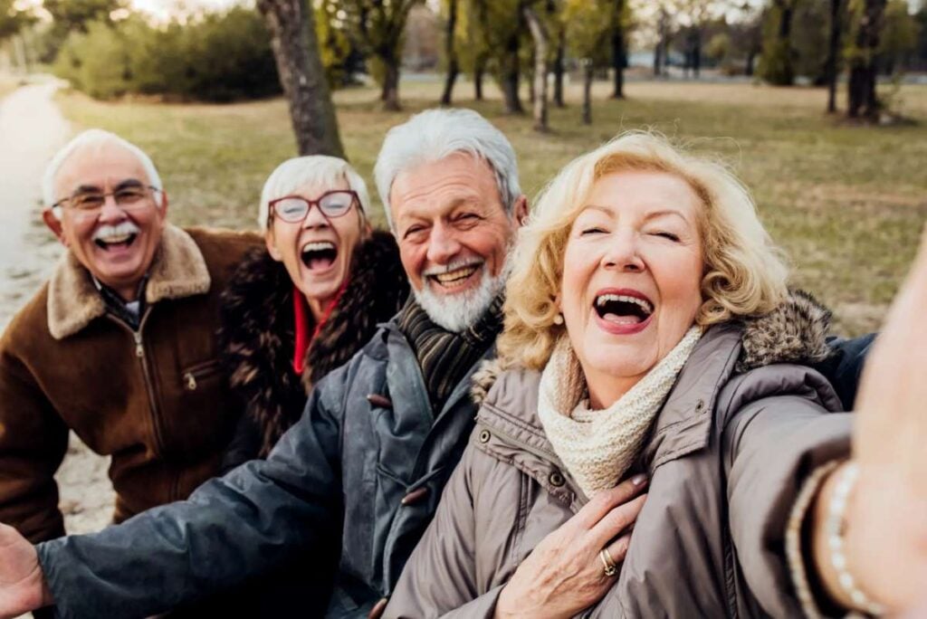 8 things the happiest people over 65 do every single day that keep them feeling young 3 Four older adults laughing together while taking a selfie outdoors in a park.