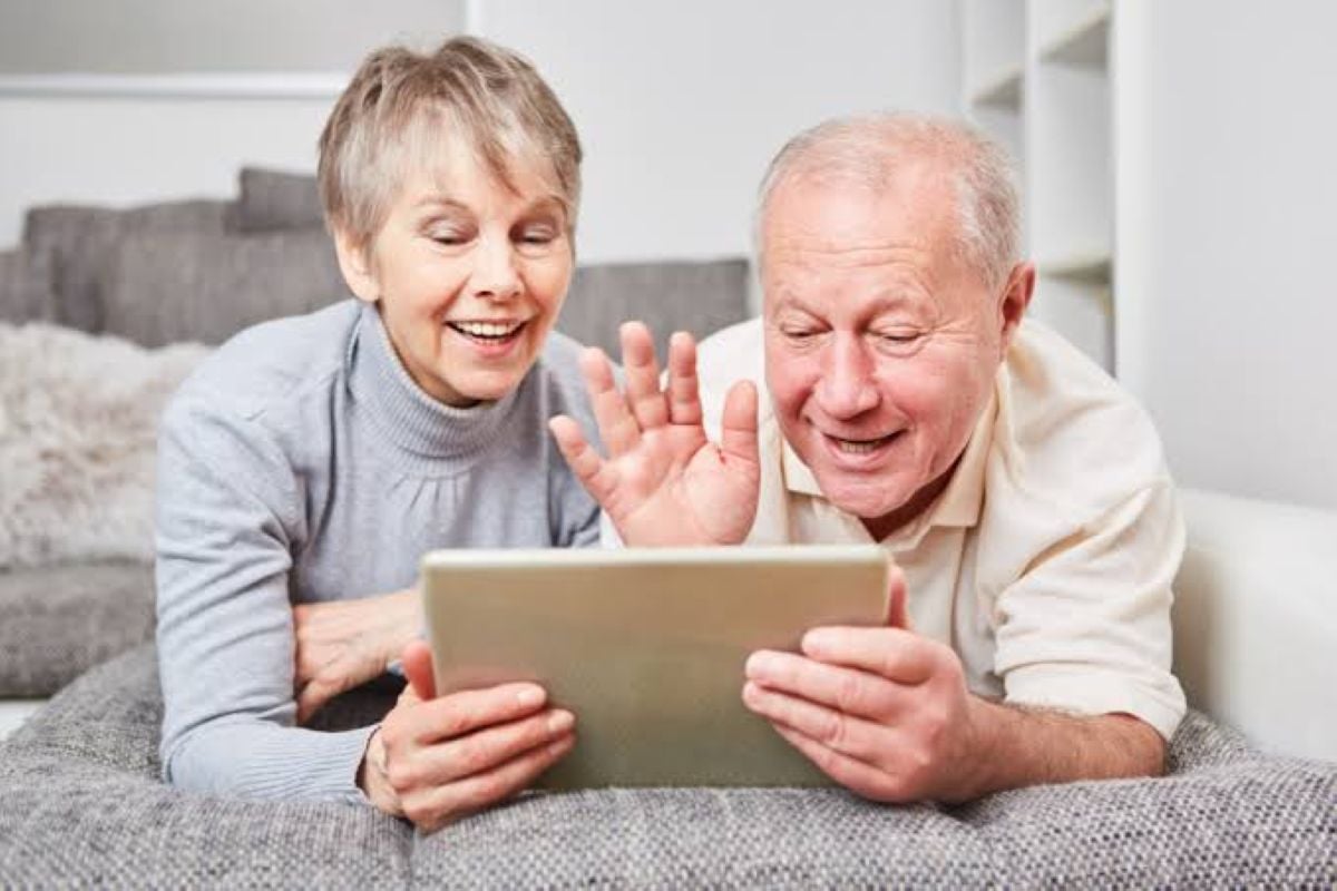 Grandparents smiling and waving at a tablet during a video call, illustrating long-distance connection with grandchildren.