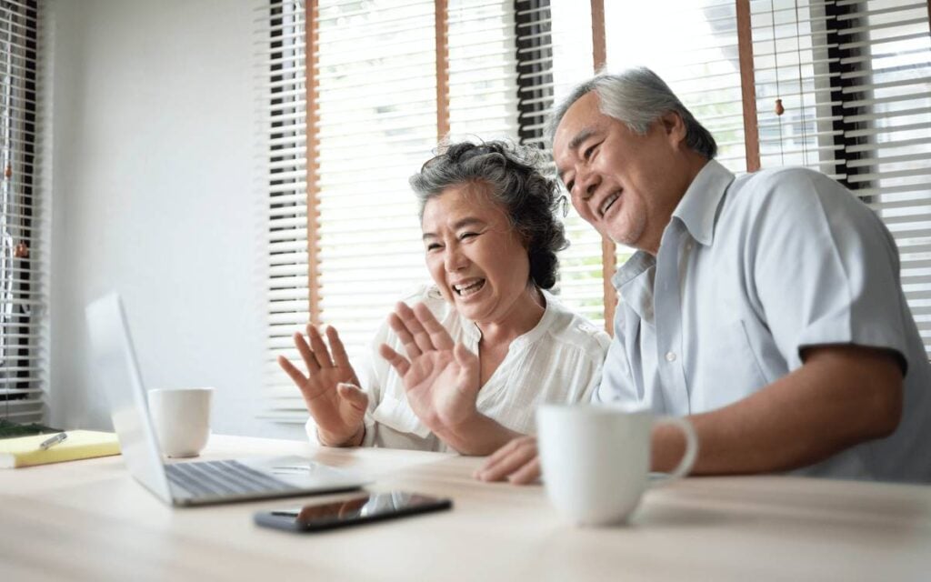 7 Simple Things Long-Distance Grandparents Can Do So Their Grandkids Never Feel Like Strangers 4 Grandparents happily waving at a laptop during a video call at home, showing a joyful long-distance moment with grandchildren.