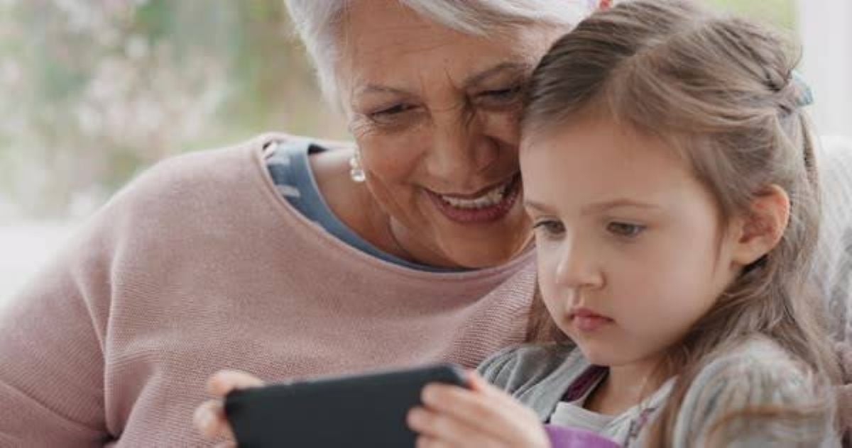 Grandmother and young granddaughter sitting together and looking at a smartphone, highlighting early exposure to social media.