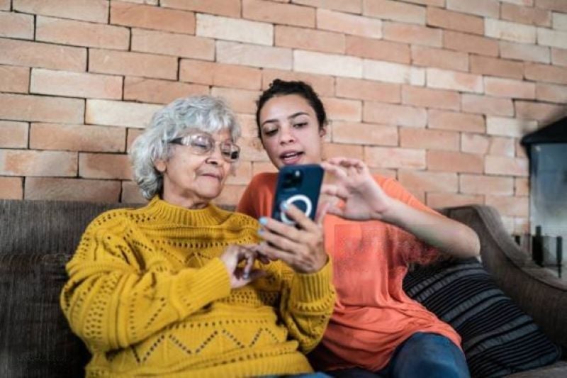 7 Ways Grandparents Can Protect Their Grandkids From the Dangers of Social Media Without Overstepping 3 Teenager showing her grandmother something on a smartphone while sitting together, illustrating guidance and shared learning about technology.