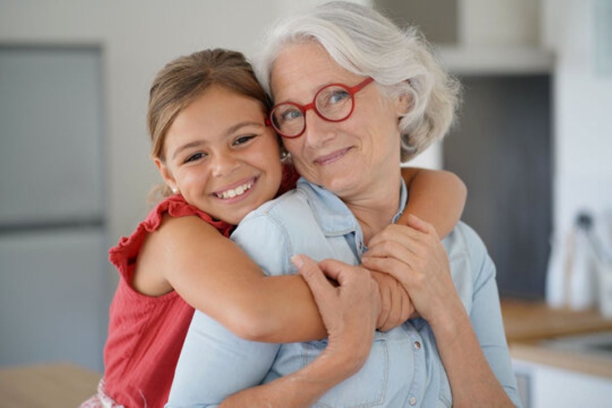 Grandmother hugging her smiling granddaughter in a warm family kitchen, showing a close and loving grandparent-grandchild relationship.
