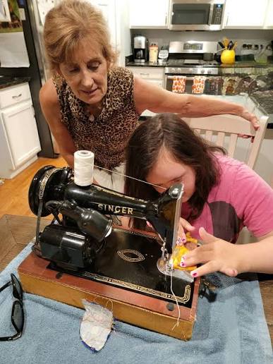 Here Are 11 Small Things You Can Do With Your Grandchild That Will Make a Huge Impact 3 A grandmother teaches her granddaughter how to sew using a vintage Singer sewing machine at the kitchen table.