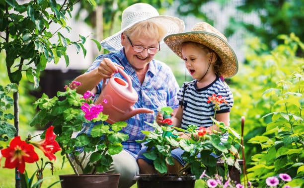 Here Are 11 Small Things You Can Do With Your Grandchild That Will Make a Huge Impact 4 A smiling grandmother and her young grandson water colorful flowers together in a sunny garden.