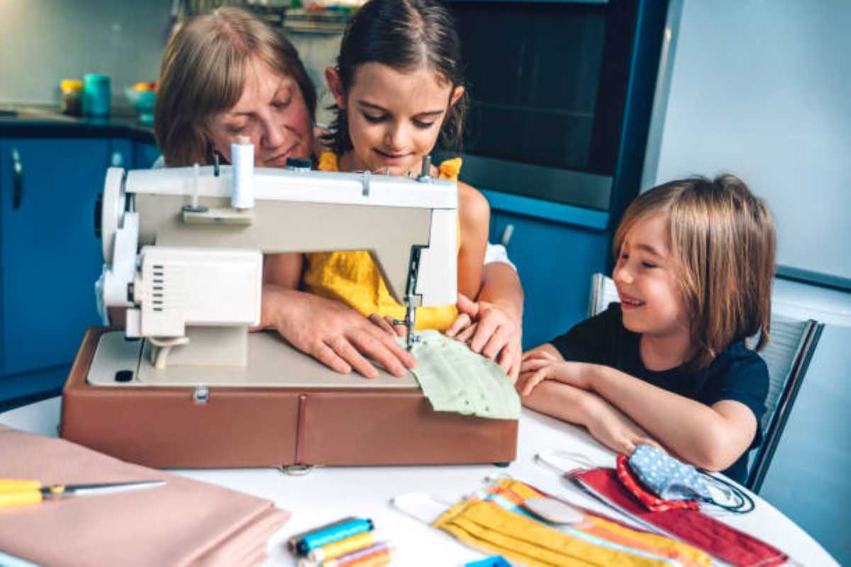 A grandmother teaches her two grandchildren how to sew with a sewing machine while spending time together at home.