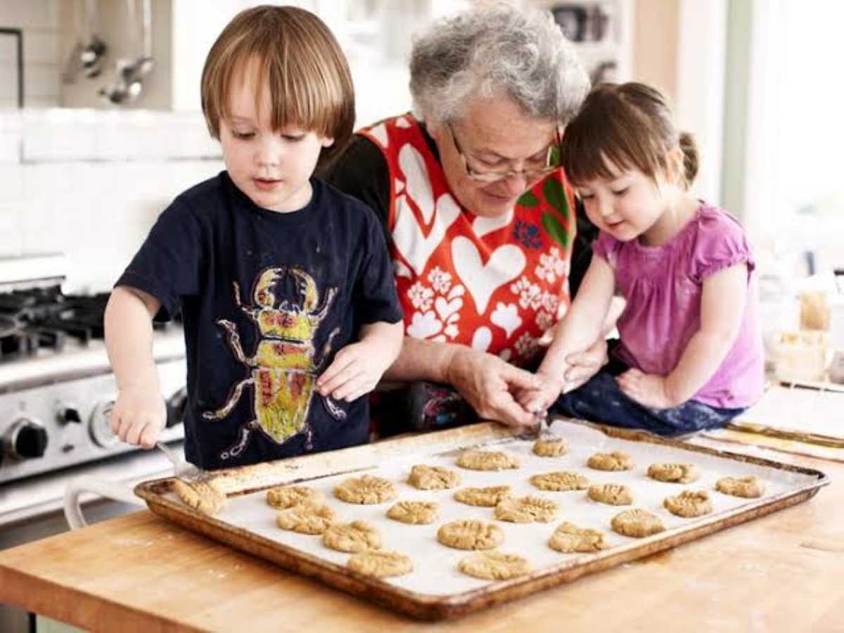 Grandmother baking cookies with her young grandson and granddaughter in a bright kitchen, sharing a warm everyday moment together.