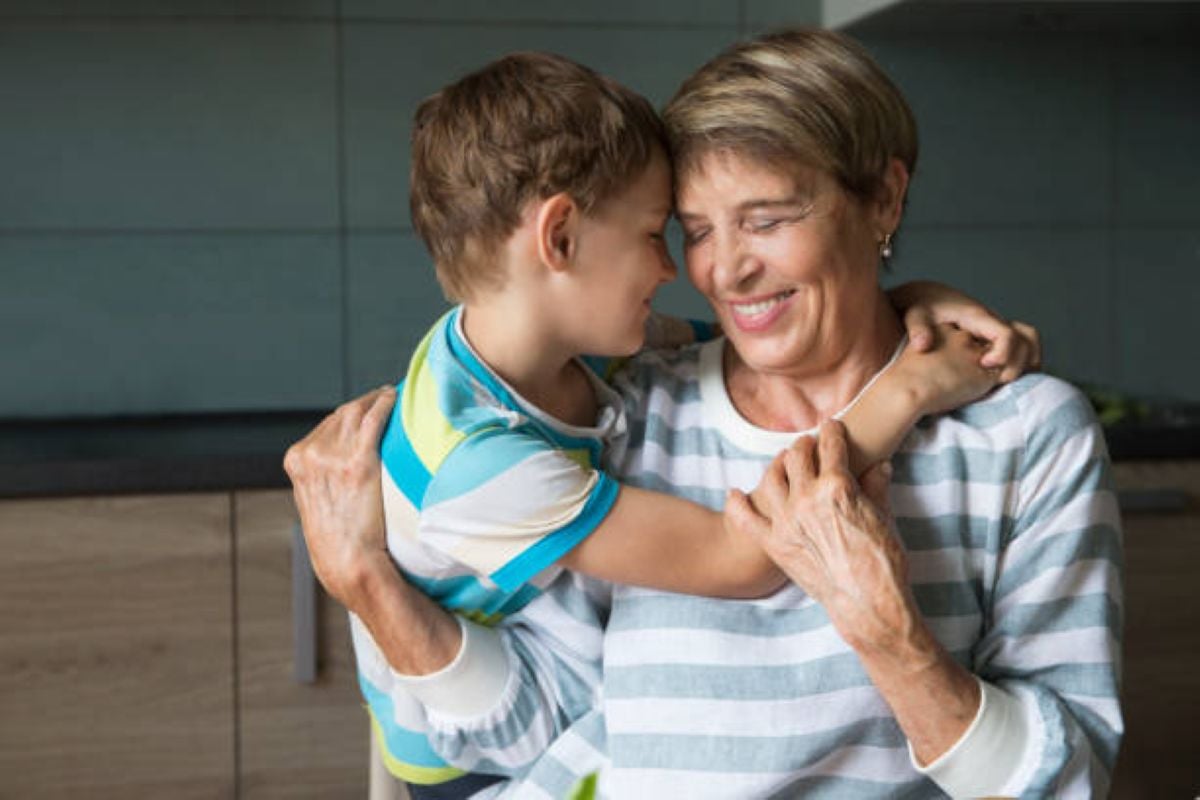 A smiling grandmother shares a warm hug with her young grandson in the kitchen, enjoying a sweet and affectionate moment together.