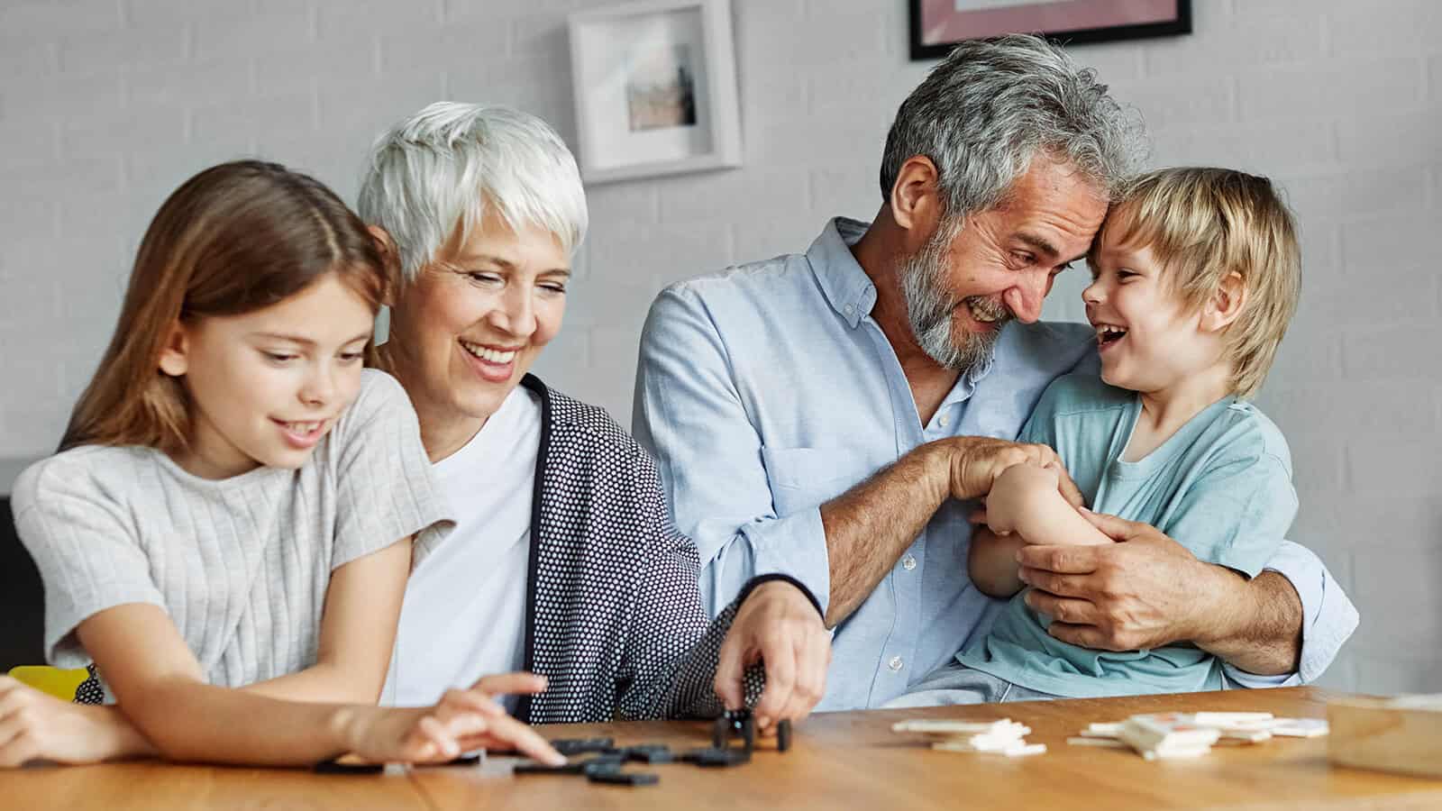 Grandparents enjoying quality time with their two grandchildren at home, playing games, laughing, and sharing precious family moments together.