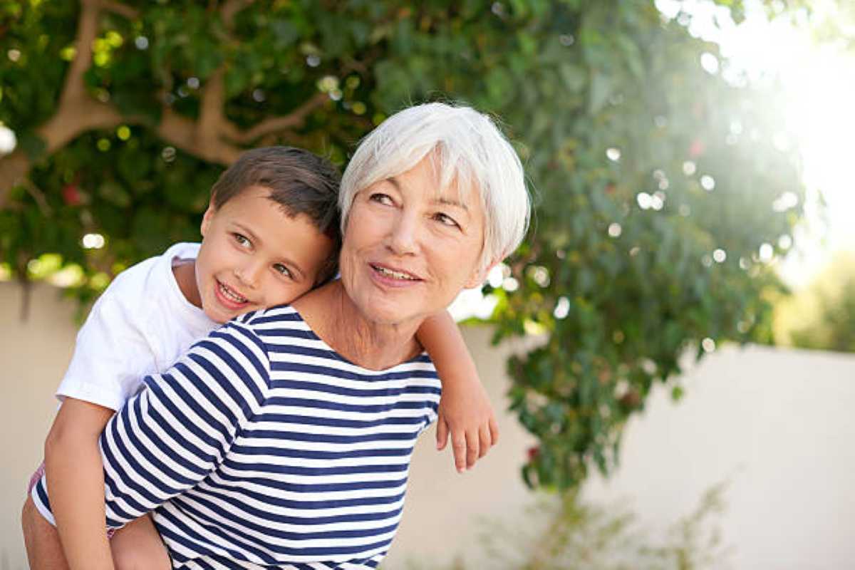 Grandmother giving her young grandson a piggyback ride outdoors as they smile and enjoy time together.